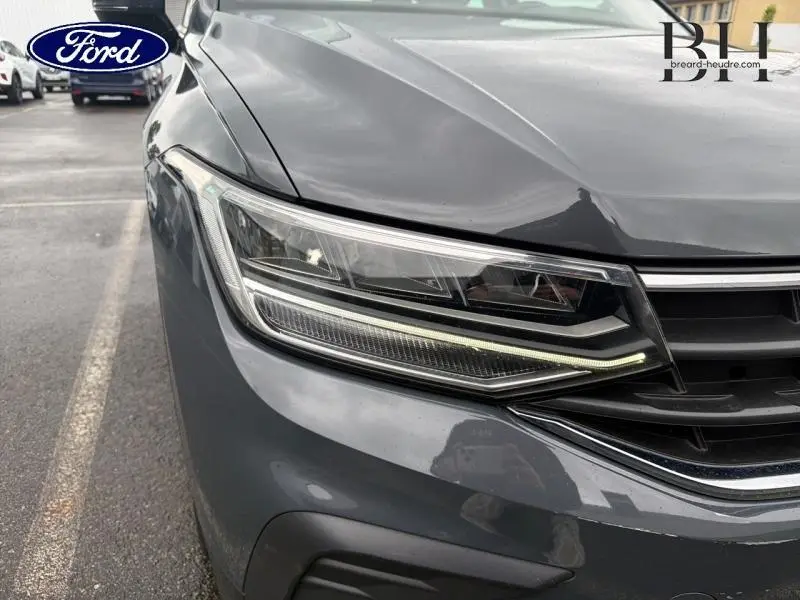 Gros plan sur le phare avant gauche du Volkswagen Tiguan gris Dauphin métallisé, soulignant les lignes LED modernes.