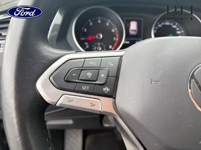 Gros plan sur le volant cuir multifonction gris d’un Volkswagen Tiguan 1.5 TSI, avec commandes de régulateur de vitesse visibles.