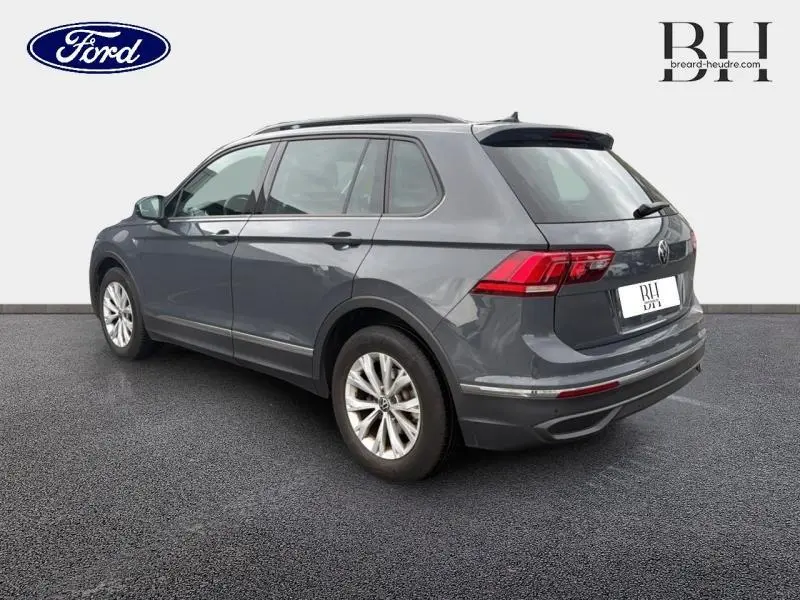 Vue 3/4 arrière droite d'un Volkswagen Tiguan gris dauphin métallisé avec barres de toit et jantes alu.