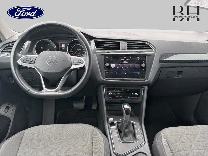 Vue intérieure avant du Volkswagen Tiguan 1.5 TSI 2021 avec tableau de bord noir, volant cuir multifonction et écran tactile central.