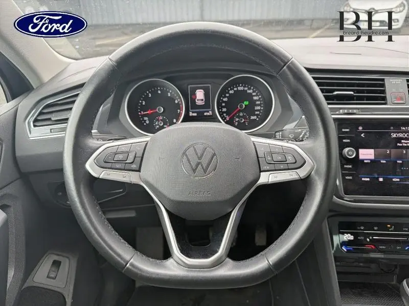 Vue intérieure centrée sur le volant cuir multifonction d'un Volkswagen Tiguan 2021, tableau de bord et écran tactile visibles.