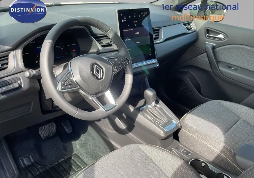 Vue intérieure de la Renault Captur 2025 montrant le volant, la console centrale avec écran tactile et les sièges tissu gris.