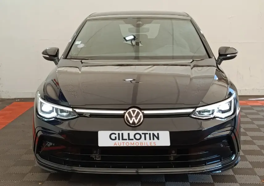 Vue frontale d'une Volkswagen Golf 1.5 eTSI noire avec phares LED allumés et logo R-Line visible sur la calandre.