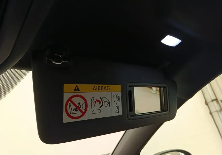 Détail intérieur du pare-soleil côté conducteur avec miroir et avertissement airbag, dans une Volkswagen Golf noire.