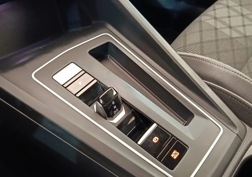 Gros plan sur la console centrale noire de la Volkswagen Golf 1.5 eTSI avec levier de vitesses automatique et boutons de frein à main électronique.