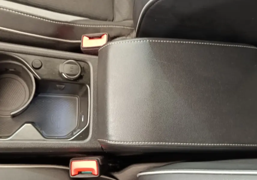 Vue rapprochée de la console centrale noire avec accoudoir cuir et zone de recharge sans fil dans une Volkswagen Golf 2021.