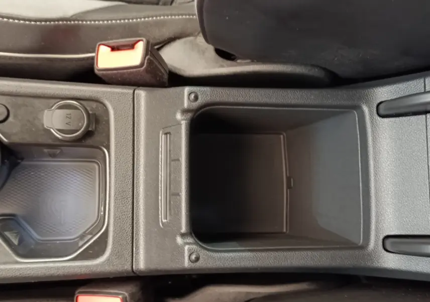 Vue plongeante sur la console centrale noire de la Volkswagen Golf 1.5 eTSI R-Line avec prise 12V et zone de recharge sans fil.