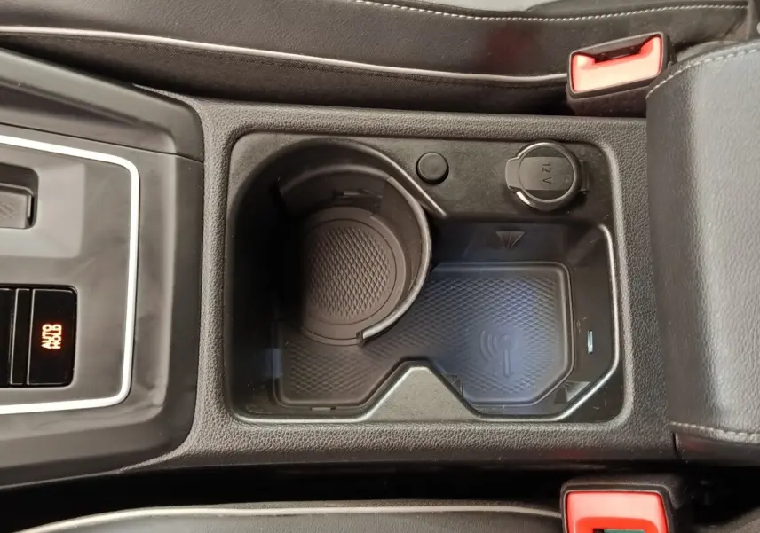 Vue rapprochée de la console centrale noire de la Volkswagen Golf 1.5 eTSI avec zone de recharge sans fil et prise 12V.
