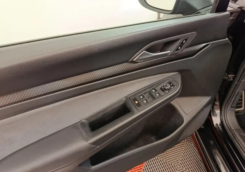 Vue rapprochée de la porte avant gauche noire d’une Volkswagen Golf 1.5 eTSI R-Line, avec commandes électriques et insert carbone.
