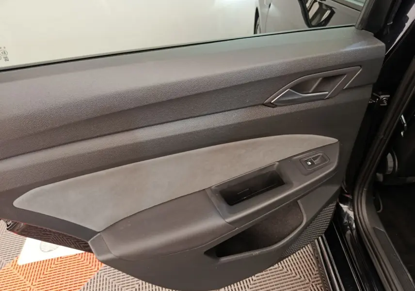 Vue rapprochée de la porte avant droite noire de la Volkswagen Golf 1.5 eTSI avec garniture grise et bouton de verrouillage.