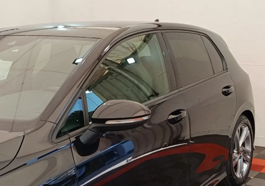 Vue côté gauche avant d'une Volkswagen Golf noire 1.5 eTSI R-Line avec jantes alliage et rétroviseur noir brillant.