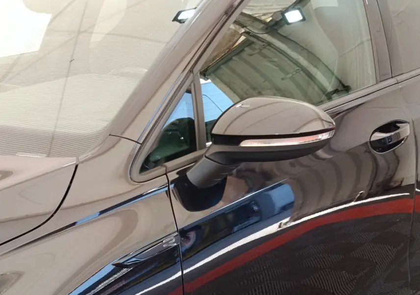 Vue rapprochée du côté gauche d’une Volkswagen Golf noire, mettant en valeur le rétroviseur et la poignée de porte.