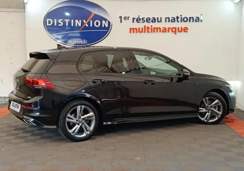 Vue de profil côté droit d'une Volkswagen Golf 1.5 eTSI noire finition R-Line avec jantes alliage, en intérieur showroom.