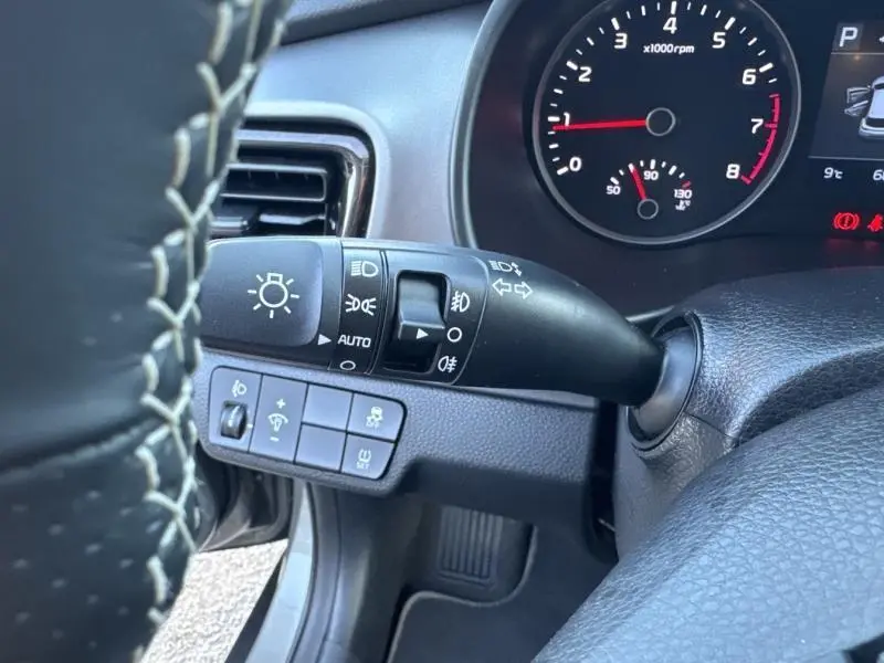 Vue rapprochée du commodo d'éclairage et du volant en cuir noir à surpiqûres blanches dans l'habitacle d'une Kia Stonic brun Sienne.