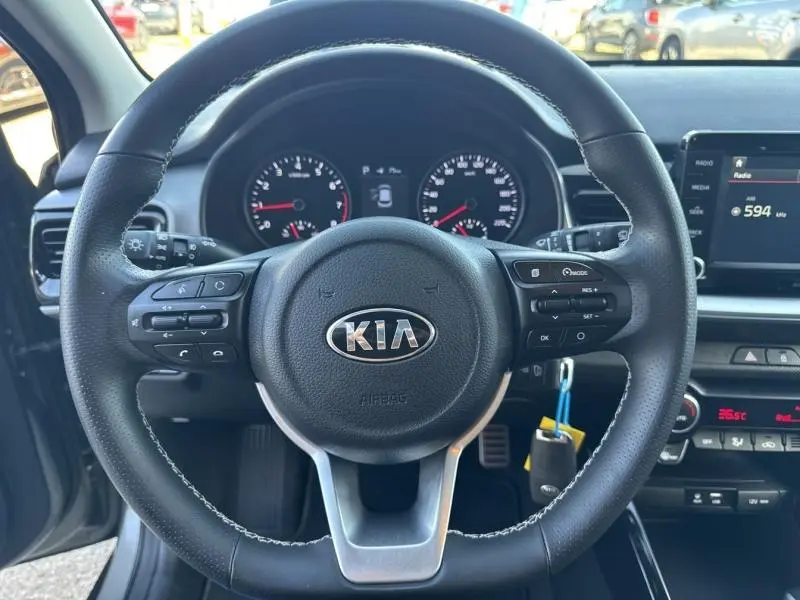 Vue rapprochée du volant cuir noir avec commandes intégrées du Kia Stonic 2019, tableau de bord et écran tactile visibles.