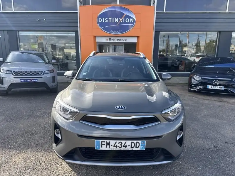Vue de face d’un KIA STONIC brun sienne avec calandre chromée, stationné devant un showroom Distinxion.