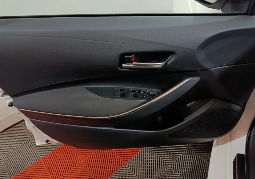 Vue intérieure de la porte avant gauche noire de la Toyota Corolla hybride 2022, avec commandes électriques et poignée chromée.