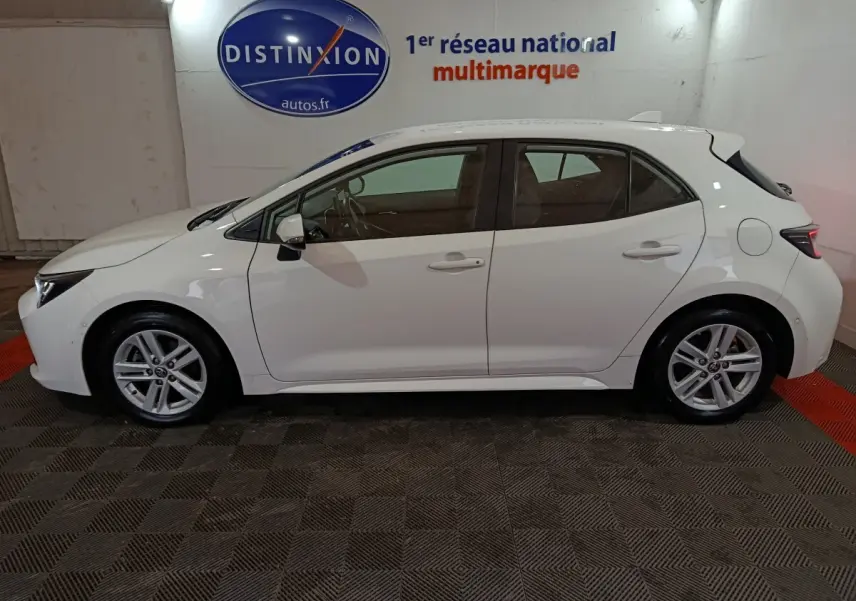 Vue de profil côté gauche d'une Toyota Corolla hybride blanche 2022, avec jantes alliage et rétroviseurs électriques.