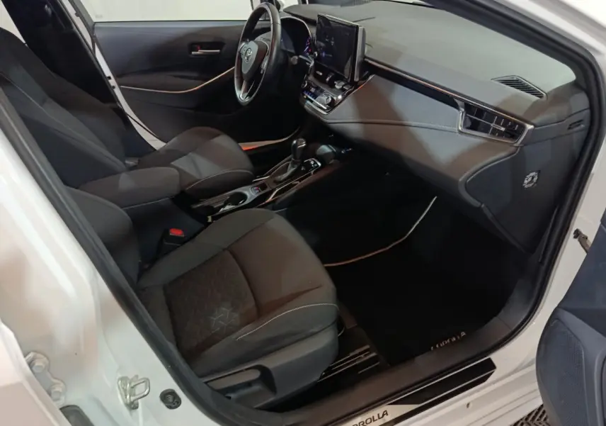 Vue intérieure côté conducteur de la Toyota Corolla hybride blanche 2022, avec tableau de bord moderne et sièges noirs.