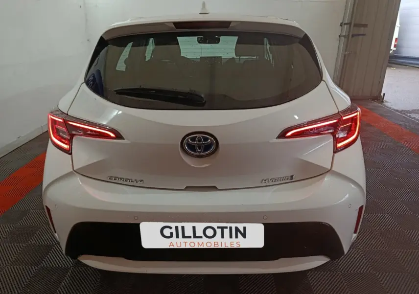 Vue arrière d'une Toyota Corolla hybride blanche avec feux arrière LED allumés dans un garage.