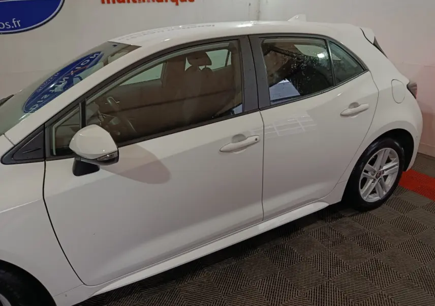 Toyota Corolla hybride blanche vue de profil côté gauche, avec rétroviseur rabattable électriquement visible.