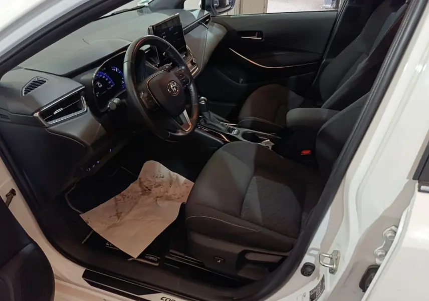 Vue intérieure côté conducteur de la Toyota Corolla hybride blanche 2022, avec tableau de bord et sièges noirs.