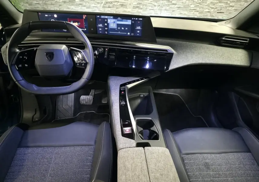 Vue intérieure avant du Peugeot 5008 2025, tableau de bord et console centrale avec finition tissu gris et noir laqué.