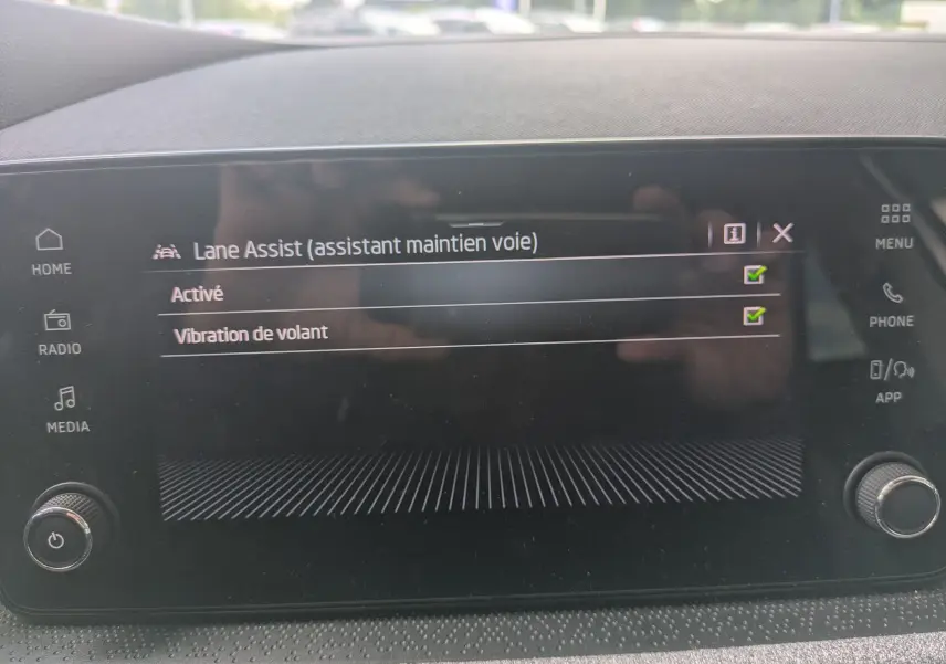 Écran tactile intérieur de la Skoda Scala gris Reflex affichant l'activation de l'assistant maintien de voie avec vibration de volant.