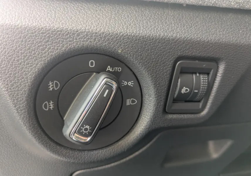 Gros plan sur le sélecteur de phares noir et chrome dans l'habitacle du Skoda Scala gris, côté gauche du tableau de bord.
