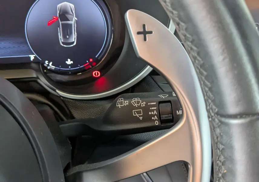 Gros plan sur le volant et le compteur digital de l'Alfa Romeo Stelvio 2023, avec palettes au volant et affichage de porte ouverte.