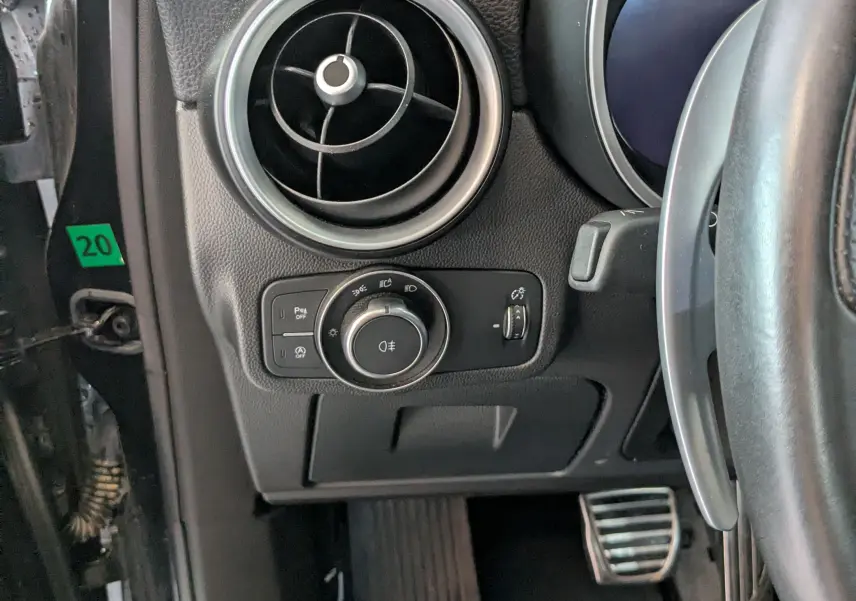 Gros plan sur la partie gauche du tableau de bord noir de l'Alfa Romeo Stelvio 2023, avec aérateur rond et commandes d'éclairage.