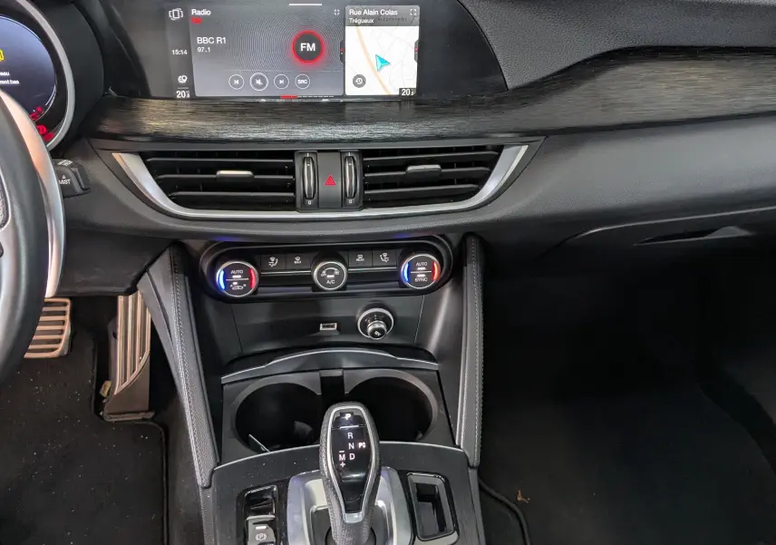 Vue intérieure centrée sur la console centrale et l’écran tactile d’un Alfa Romeo Stelvio noir 2023 avec finition bois sombre.