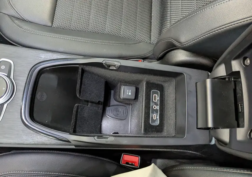 Gros plan sur la console centrale noire de l'Alfa Romeo Stelvio 2023, montrant la station de charge sans fil et ports USB/AUX.