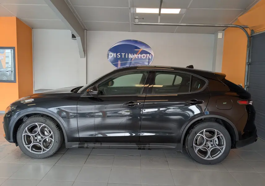 Profil côté gauche d'un Alfa Romeo Stelvio noir 2023, avec jantes alliage 19 pouces et hayon arrière visible en intérieur showroom.
