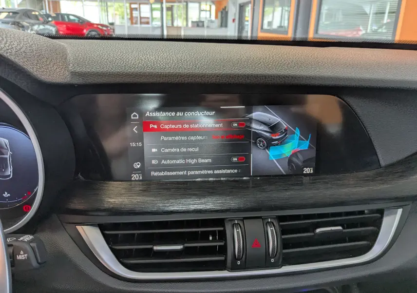 Écran central de l'Alfa Romeo Stelvio noir 2023 affichant l'assistance au conducteur avec capteurs et caméra de recul.