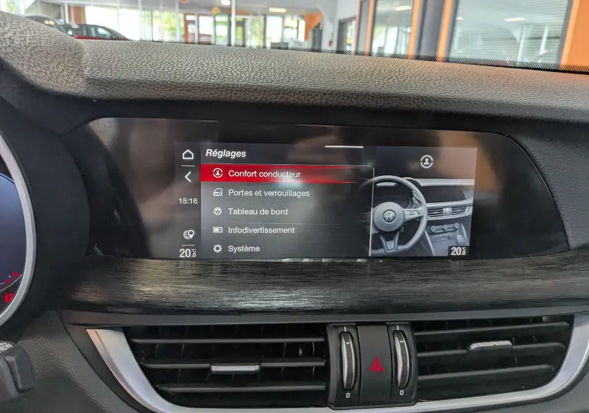 Écran tactile central du tableau de bord de l'Alfa Romeo Stelvio 2023 affichant les réglages, avec finition bois et aérateurs noirs.