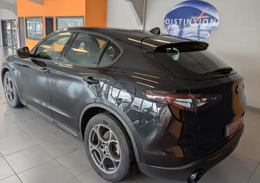 Vue 3/4 arrière côté gauche d'un Alfa Romeo Stelvio noir 2023 avec jantes sport et feux LED trilobe.