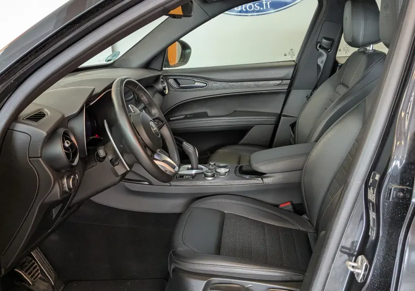Intérieur côté conducteur d'un Alfa Romeo Stelvio noir 2023, sièges technocuir noirs et tableau de bord moderne.
