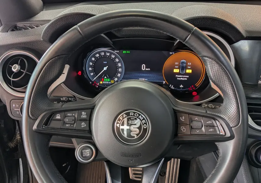 Vue intérieure centrée sur le volant cuir noir de l'Alfa Romeo Stelvio 2023 avec tableau de bord digital et commandes intégrées.