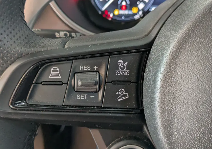 Gros plan sur le volant noir de l'Alfa Romeo Stelvio 2023, avec commandes de régulateur et bouton start/stop visibles.