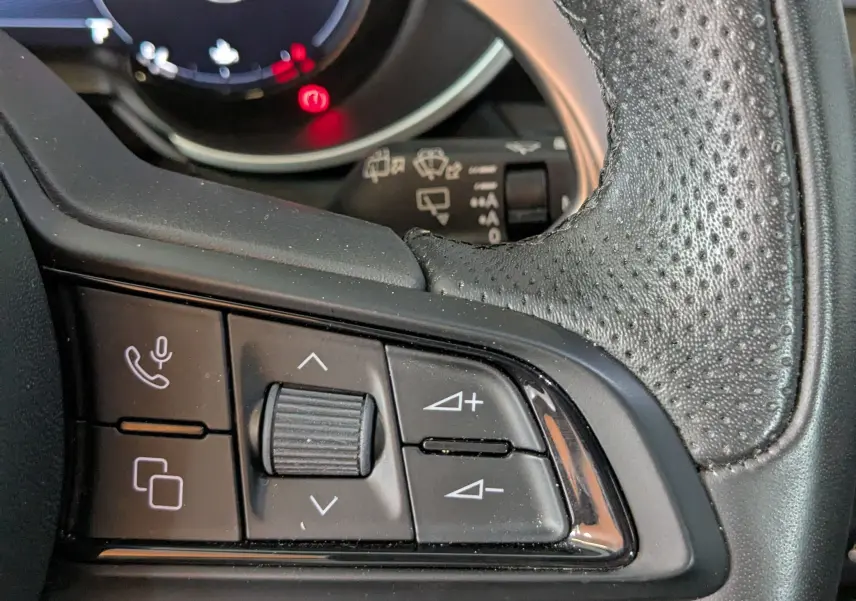 Gros plan sur les commandes du volant en cuir noir perforé de l'Alfa Romeo Stelvio 2023, affichage numérique en arrière-plan.