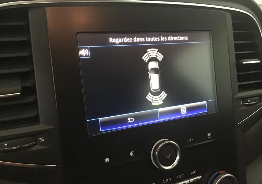 Écran central de la Renault Mégane IV Berline blanc montrant l'alerte de détection d'obstacles en mode stationnement.