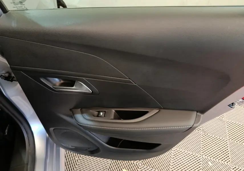 Porte intérieure côté gauche gris clair de la Peugeot 208 PureTech 100 S&S Allure avec poignée argentée et commande de vitre.