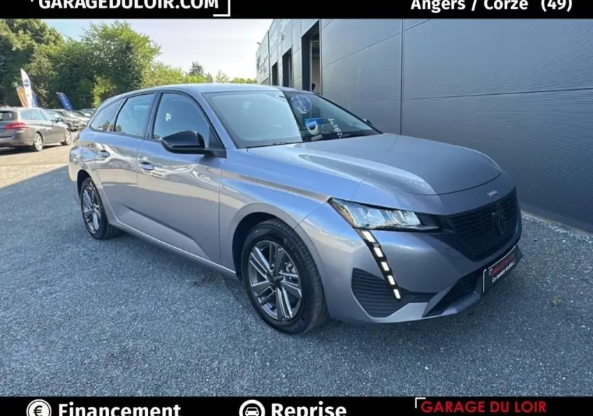 Peugeot 308 gris clair vue 3/4 avant droit, avec feux LED verticaux et jantes alliage distinctives.