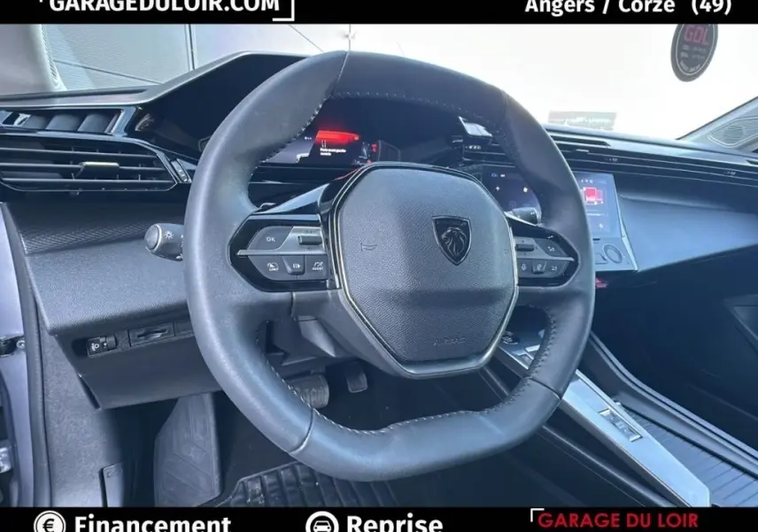 Vue intérieure centrée sur le volant cuir de la Peugeot 308 gris clair, avec tableau de bord digital et console tactile visible.