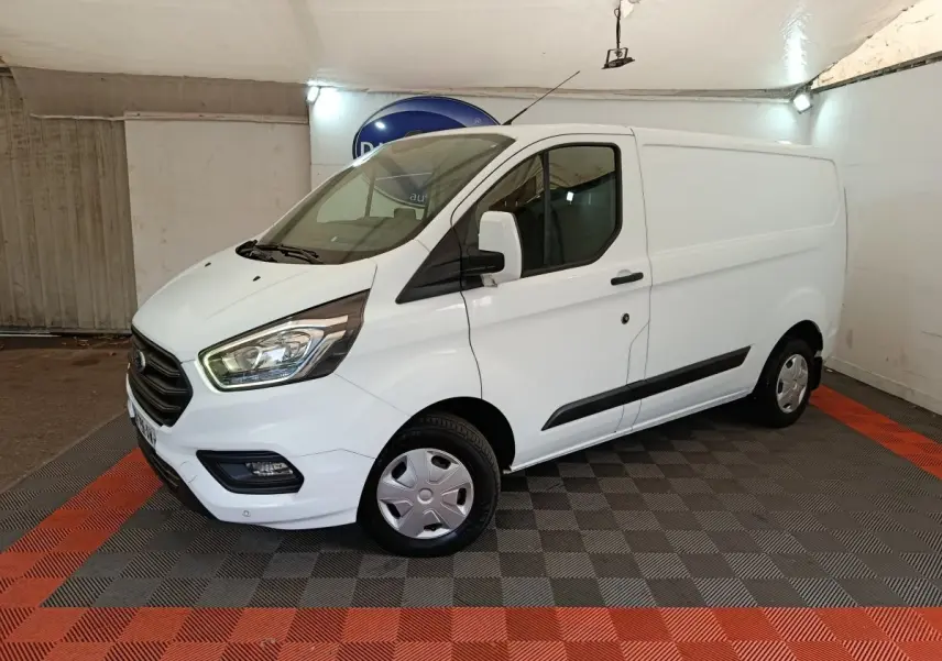 Vue 3/4 avant droit d'un fourgon Ford Transit Custom blanc avec calandre noire et feux avant allumés.