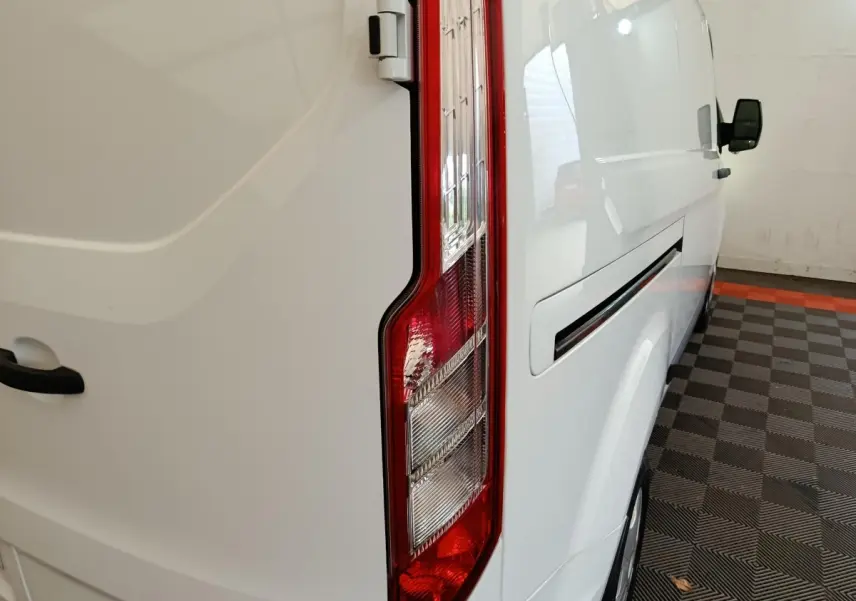 Vue arrière côté droit du fourgon blanc Ford Transit Custom avec feu arrière vertical et poignée de porte visible.