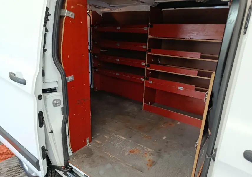 Vue intérieure côté droit du fourgon Ford Transit Custom blanc, montrant les étagères rouges de rangement.