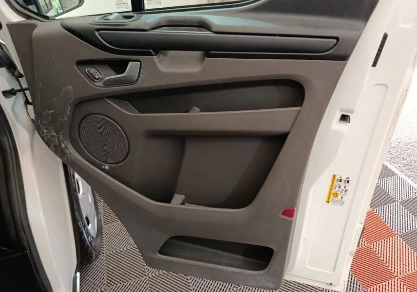 Vue intérieure côté gauche de la porte avant blanche du Ford Transit Custom Fourgon avec panneau noir et haut-parleur intégré.