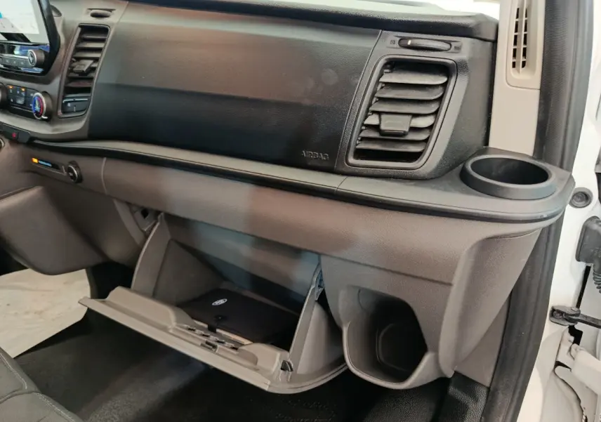 Vue intérieure côté passager du tableau de bord gris et noir du Ford Transit Custom avec boîte à gants ouverte et porte-gobelet.